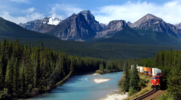 Heavily loaded freight train crosses beautiful Canadian landscape repreezenting green freight