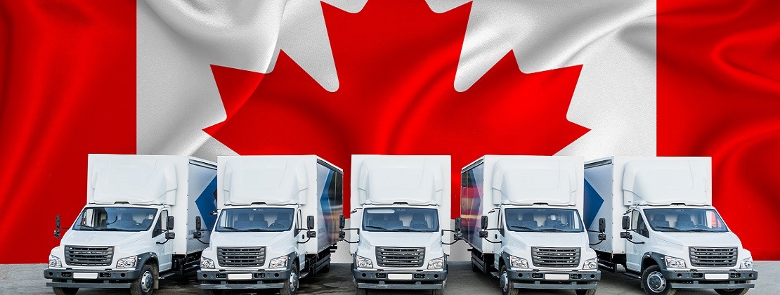 Canada flag in the background. Five new white trucks are parked in the parking lot.