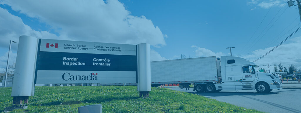 A Canada Border Security billboard with a freight truck behind it.