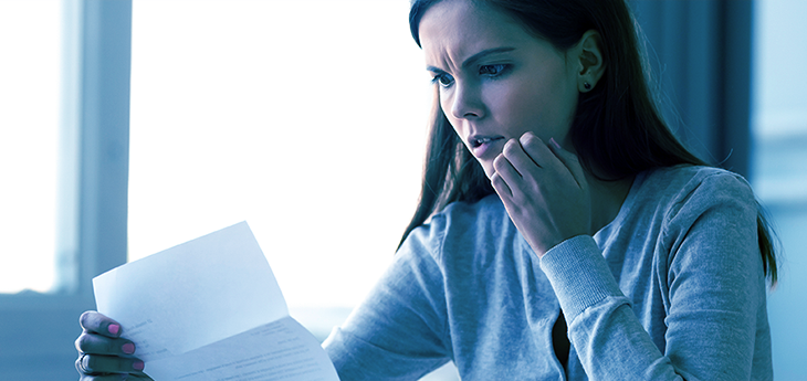 Woman looking at a piece of paper with a worried expression.